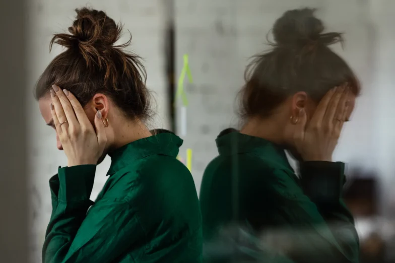 Woman covering her face next to a blurred reflection, illustrating dissociation and mind-body disconnection in trauma.