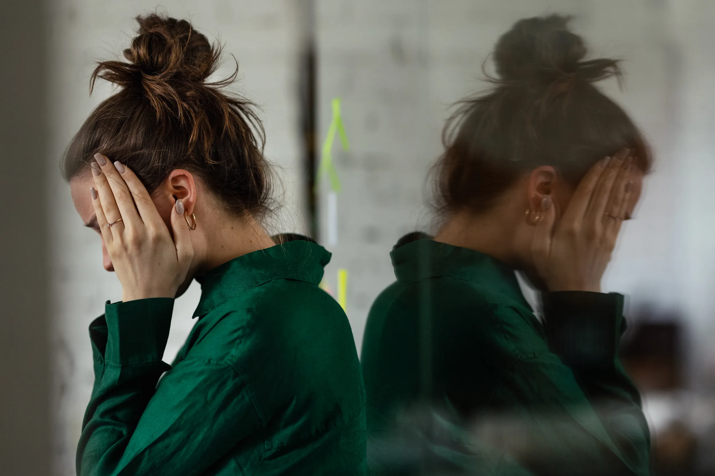 Woman covering her face next to a blurred reflection, illustrating dissociation and mind-body disconnection in trauma.