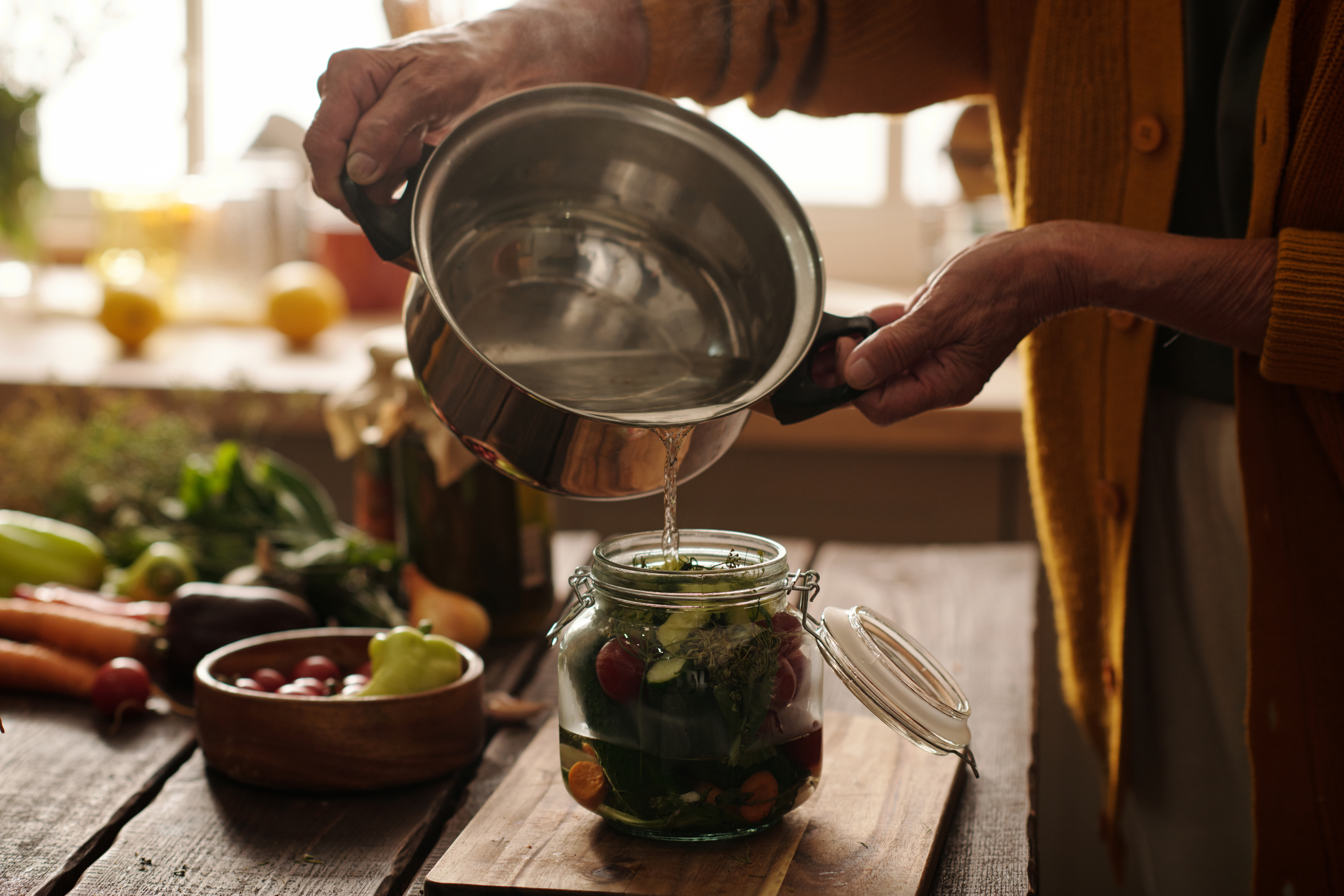 Hands of senior woman with pan pouring hot water into jar with vegetables