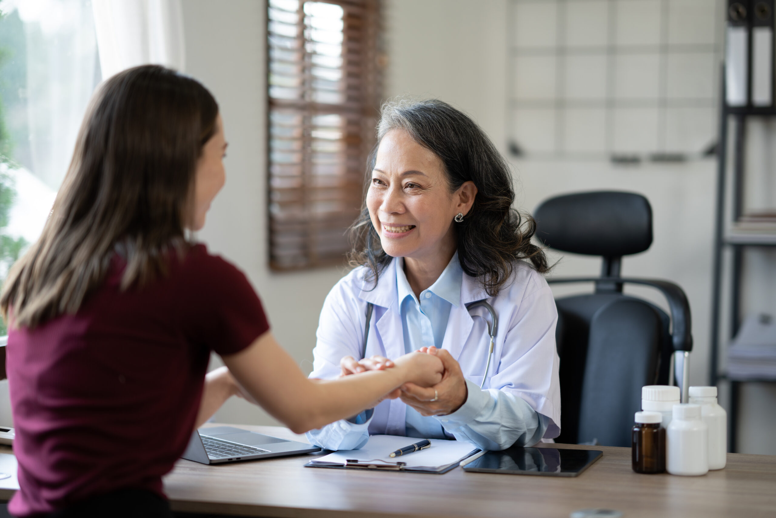 Positive senior medical professional, doctor, nurse giving support and help to young female patient at appointment.
