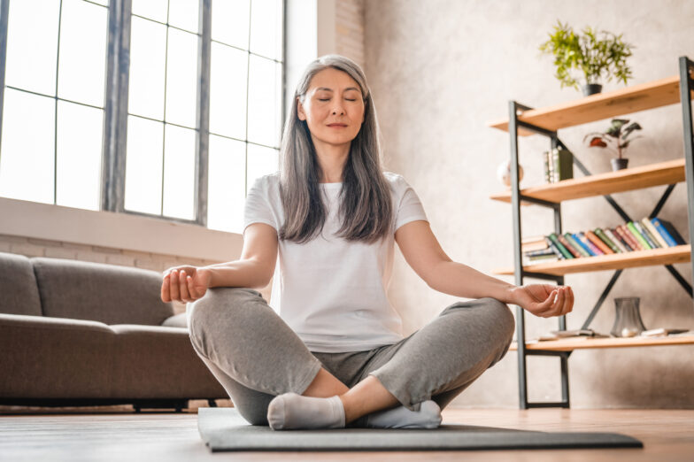 woman practicing mindfulness meditation at home, sitting cross-legged with eyes closed—supporting emotional healing and chronic pain management through gentle awareness.