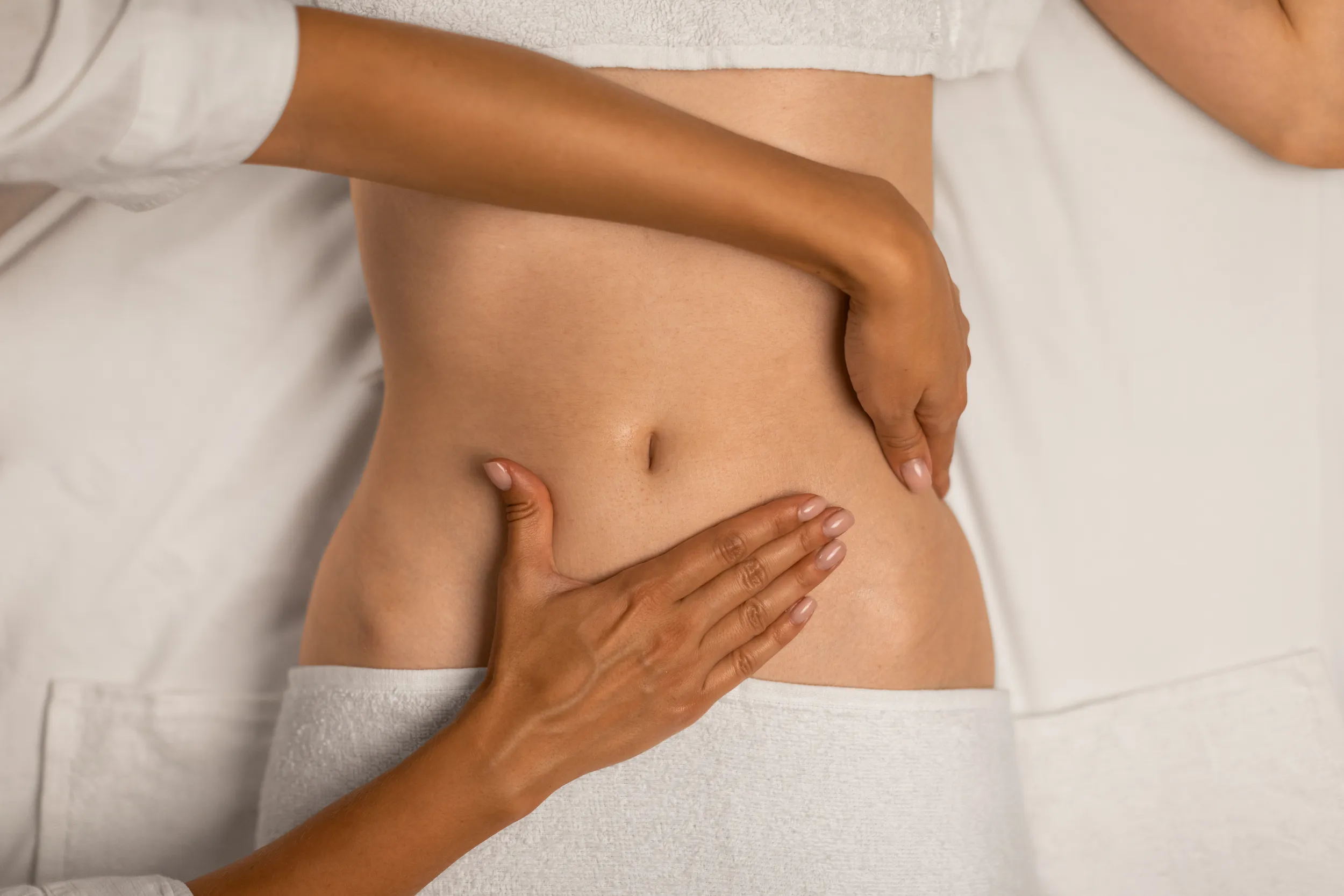 Close-up of a practitioner&rsquo;s hands performing manual therapy on a woman&rsquo;s lower abdomen while she lies on a treatment table.